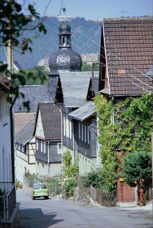 steile Dorfstraße, beidseitig Häuser, Kirchturmspitze
