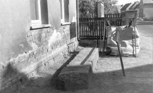 Krauschwitz-Keula. Wohnhaus an der Kapelle, davor Granitstein einer ehem. Hirsestampfe