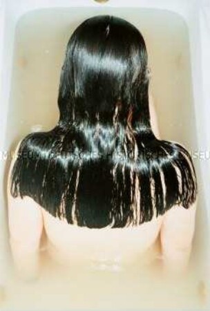 Rückenansicht einer jungen Frau mit schwarzen Haaren in der Badewanne (Altersgruppe 18-21)