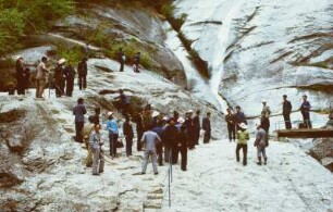 Reiseteilnehmer auf einem Felsen vor einem Wasserfall stehend