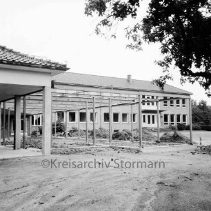 Volksschule [später Emil-Nolde-Schule]: am Schweinemarkt: Erweiterungsbau: Pausenhalle in Bau: Fundamente, Stahlkonstruktion: Erdhaufen: links bislang offene Wangelgalerie: im Hintergrund Klassentrakt: rechts oben Zweige eines Baumes