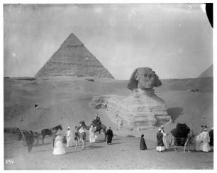 Gizeh (Ägypten): Kamelkarawane vor der Sphinx von Gizeh. Einheimische mit Kamelen. Touristen mit Einspänner vor der Sphinx von Gizeh