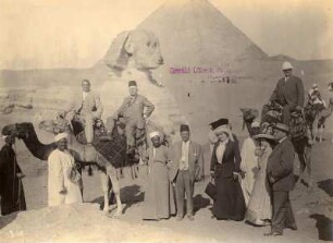 Gizeh (Ägypten). Touristen und einheimische Führer mit Kamelen vor der Sphinx und den Pyramiden von Gizeh