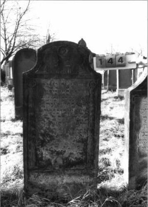 Grabstein 144 (Index: 100116320) Material: Sandstein Zustand: gut Maße HxBxT: 142x65x17 cm Beschreibung: Stele mit konkav eingezogenem Segmentbogenabschluß, eingetieftes Schriftfeld Symbolik: Ranken, Rosette: Grabstein 144