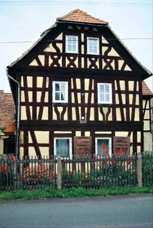 Giebelansicht des Bauernhauses von Bild 13, sehr eng stehendes Fachwerk, Denkmal; Vorgarten zur Straße hin mit Staketenzaun