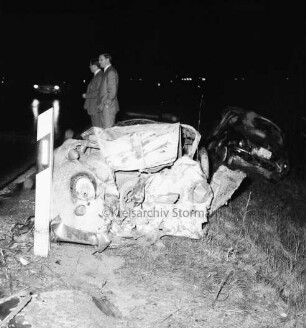 B 404: bei Herrenhaus Nütschau: Verkehrsunfall: Zusammenstoß von zwei Pkws und Auffahrunfall: am Straßenrand ausgebrannter Unfallwagen VW Karmann-Ghia nach Löschen, Leitpfosten: dahinter zwei Männer: hinten rechts Unfallwagen in Straßengraben: im Dunkeln, 1. Mai 1967