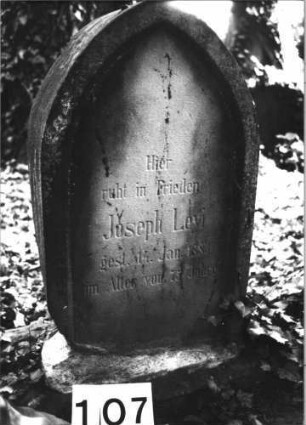 Grabstein 107 (Index: 100085527) Zustand: rechter Teil Rückseite weggebrochen Maße HxBxT: 75x50x23 cm Beschreibung: Stele, Sockel, Spitzbogenabschluß, Schriftfeld eingetieft auf Vorderseite: Grabstein 107