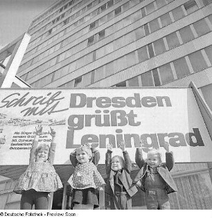Dresden-Altstadt, Ostra-Allee 20. Jubelnde Kleinkinder vor dem Aufsteller zur Aktion "Schreib mit! Dresden grüßt Leningrad" am Haus der Presse
