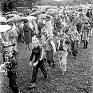 Kindervogelschießen: Festwiese: Festumzug: Schulkinder in Cowboy- und Indianerkostümen: hinten Zuschauer mit Regenschirmen: im Hintergrund Häuser und Bäume