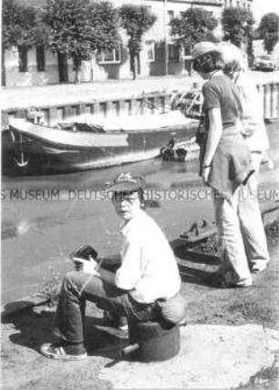 Junge mit Mütze sitzt an einem Fluss (Altersgruppe bis 14)