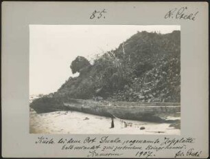 An der Küste bei Douala, Kamerun : zerbrochenes Kanu, das auf einem Sandstreifen vor einem bewachsenen Hügel liegt