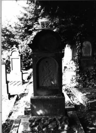 Grabstein 32 (Index: 99801980) Material: Sandstein Zustand: hebräische Schrifttafel fehlt Maße HxBxT: 134x50x25 cm Beschreibung: Stele, getreppter Sockel, eingezogener Rundbogenabschluß mit Verdachung, eingetieft. Schriftfeld mit Rundbogen Symbolik: achtzackiger Stern, Blätter: Grabstein 32