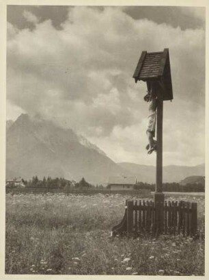 Bei Garmisch. Die Zugspitze vom Garmischer Talkessel gesehen. Im Vordergrund ein Kruzifix auf einer blühenden Sommerwiese