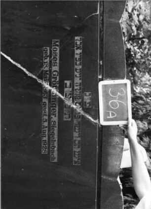 Grabstein 36 (Index: 99753482) Material: Granit Zustand: gebrochen und repariert Maße HxBxT: 125x133x15 cm Beschreibung: Stele breit, Sockel, Korbbogenabschluß mit Eckakroteren Besonderheit: kulturhistorisch wertvoll / hist.-wiss. Gründe (Gemeindestellun): Grabstein 36A
