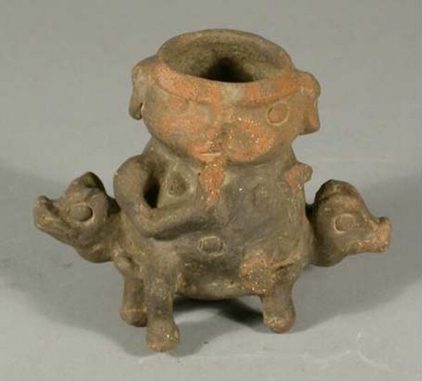 Shape of a female figure, sitting on a stool with animal heads