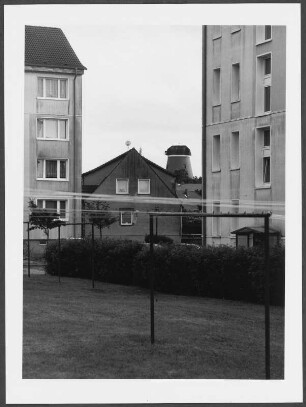 Blick auf einen Wäscheplatz vor Wohnhäusern, im Hintergrund ein Mühlenkörper ohne Haube, signierter Barytabzug