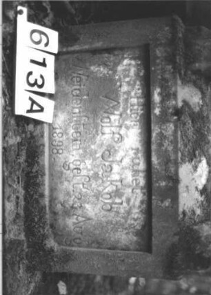 Grabstein 613 (Index: 99900673) Material: Sandstein Zustand: angewittert, Schrifttafel nicht erhalten Maße HxBxT: 156x54x26 cm Beschreibung: aufgesockelte Stele mit Giebelaufsatz, in der Mitte rechteckig erhöht, oberer Abschluss mit Scheibenfries, im Giebelfeld Blüten, Schriftfeld von Säulen gerahmt, Schrifttafel herausgebrochen und verloren Symbolik: Scheibenfries, Blüten: Grabstein 613A