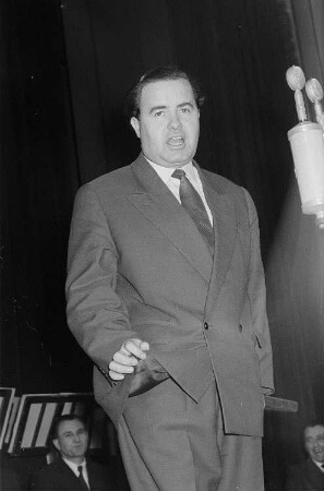 Portrait Heinz Quermanns während eines Auftritts bei der Ziehung der 52. Spielwoche des VEB Zahlenlotto, im Hintergrund Mitglieder des Rundfunk-Blasorchesters Leipzig