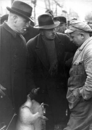 Heide. Viehmarkt. Das Ferkel lebt noch, doch der nahe Tod steht ihm bevor. Hier wird sicherlich zwischen den drei Herren der Preis verhandelt. Aufgenommen 1935