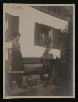 Carl Jacob Burckhardt sitzt rauchend vor einem Haus, daneben steht eine junge Frau