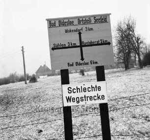 Wegweisertafel und ein Verkehrsschild "Schlechte Wegstrecke" (unten), Winterbild