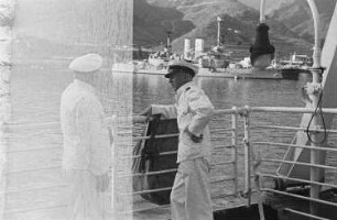 Reisefotos Mittelmeer. Passagierschiff "Milwaukee" vor Anker. Zwei Besatzungsmitglieder an der Reling. Blick zu einer Hafenstadt vor Bergkette