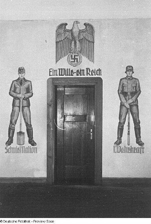 Dresden-Pirnaische Vorstadt, 18. Volksschule, Tür umrahmt von Wandmalerei. Über der Tür Adler mit dem Hakenkreuz, darunter Schriftzug: "Ein Wille - ein Reich". Rechts und links der Tür Soldaten mit Beischriften "Schule der Nation" und "Wehrkraft"