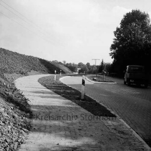 Straßenbau: Oldesloer Straße: Ausbau: Ortseingang mit Verkehrsinsel und Radfahrweg: rechts Lkw: dahinter Bäume