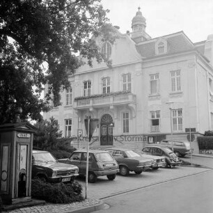 Rathaus: Paul-von-Schoenaich-Straße: Außenaufnahme: vorne Bergstraße, Parkplatz mit Autos, Verkehrsschilder, links Baum: vorne links Fleckenspumpe [Handpumpe zur Wasserversorgung] mit Schild "1842"
