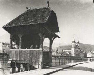 Luzern. Schweiz. Zugang zur, um 1365 als Wehrgang errichteten Kapellbrücke vom Rathaussteg gesehen. Rechts im Bildhintergrund die barocke Jesuitenkirche St. Franz Xaver mit ihren imposanten Zwiebeldoppeltürmen