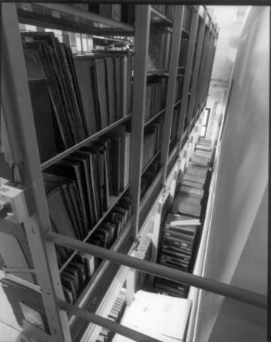 Sächsische Landesbibliothek - Staats- und Universitätsbibliothek Dresden. Zentralbibliothek (ehem. Landesbibliothek). Erdgeschoss (Flachbau). Abteilung Benutzung, Magazin. Blick vom aufgeständerten Zwischenboden nach unten auf gestapelte Bestände : Dresden-Neustadt, Marienallee 12. Sächsische Landesbibliothek - Staats- und Universitätsbibliothek Dresden. Zentralbibliothek (ehem. Landesbibliothek). Erdgeschoss (Flachbau). Abteilung Benutzung, Magazin. Blick vom aufgeständerten Zwischenboden nach unten auf gestapelte Bestände