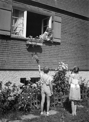 Kinderbilder. Zwei Kinder in einem Hausgarten, ein drittes aus dem Fenster schauend