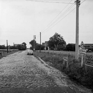 Alte Landstraße zwischen Siek und Rahlstedt: Abzweigung nach Papendorf: Kopfsteinpflaster in Richtung Siek: rechts Straßenschilder und Strommast: hinten Pkw: im Hintergrund Häuser und Bäume
