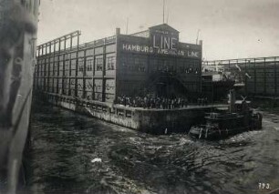 Hoboken (New Jersey), Hafen. Neues Reedereigebäude (1900-1906) Pier 1 der HAPAG - Hamburg-Amerika Linie (HAL) mit Zuschauern. Blick von einem auslaufenden Ozeandampfer (links angeschnitten)