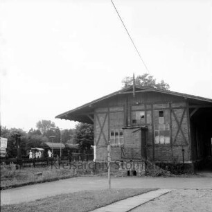 Bahnhofsgelände: Betriebsgebäude von Güterbahnhof: hinten links Bahnsteig, Reisende, Güterzug