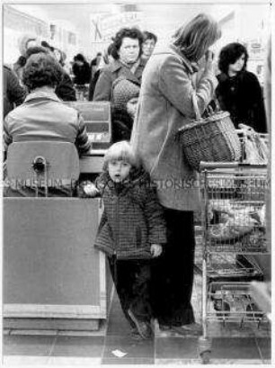 Kind mit Mutter an der vollen Supermarktkasse (Altersgruppe bis 14)