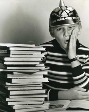 Illustration des Fotografen zu seiner Untersuchung zu Schulgeschichtsbüchern. Es zeigt einen Stapel Lehrbücher und einen Jungen mit Pickelhaube