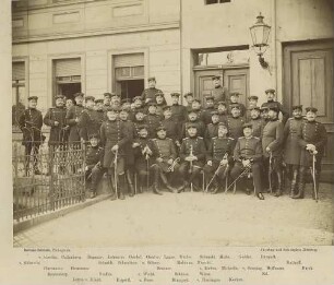 Teilnehmer (ca. neununddreissig Personen) am Lehrkurs der Feldartillerie-Schiessschule Jüterbog vor Gebäude der Schiessschule teils stehend, teils sitzend
