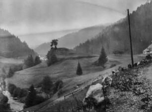 Berglandschaft : Blick auf Waldflächen auf dem Bergrücken rechts und links, sowie einen Bach links und Felsen rechts im Vordergrund