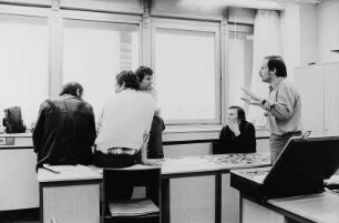 Bei einer Besprechung. Auf dem Tisch liegen zahlreiche Fotografien