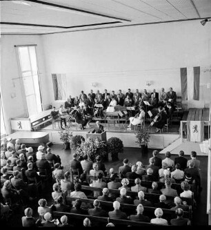 Tag der Deutschen Einheit: Feierstunde: Veranstalter Kuratorium "Unteilbares Deutschland": Theodor-Mommsen-Schule: Hamburger Straße: Festsaal: Blick von Empore: Bürgerworthalter Willy Rosch hält Ansprache: auf der Bühne Orchester der Theodor-Mommsen-Schule und Männerchor: Fahne der Bundesrepublik Deutschland, Fahne der Stadt Berlin: Gäste, 17. Juni 1961
