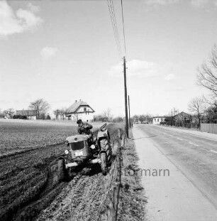 Dorfstraße: rechts die Fahrbahn, links ein Trecker auf einem Feld