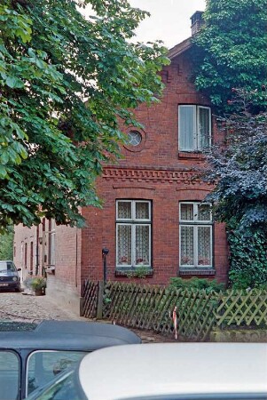 Lohe (18): giebelständiges Bauernhaus aus Backstein: Straßenfront Wohntrakt: Traufseite, von vorne Wohntrakt, Eingangstür, Wirtschaftstrakt: links Hofeinfahrt mit Kopfsteinpflaster: vorne Jägerzaun