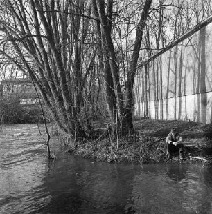 Trave: vorn rechts Angler am Ufer: dahinter Johannes Ströh Mühlenwerke (Weizenmühle): links Bäume: im Hintergrund Gebäude