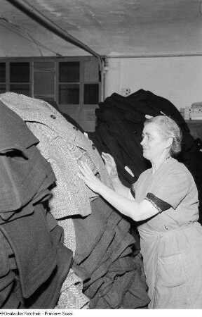 Portrait einer Frau beim Stapeln von Trenchcoats im VEB Bekleidungswerk Leipzig