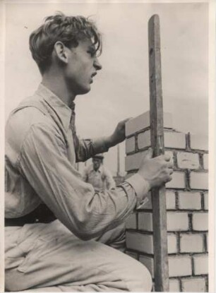 Ein Maurer überprüft mit einer Wasserwaage das Lot der Mauer