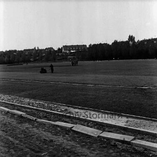 Kurpark-Stadion: Am Kurpark: Neubau: Anlegen der Rasenfläche: hinten links Mann mit Walze, rechts dahinter Männer mit Motorrasenmäher: dahinter Wohnblocks am Meisenweg zwischen Bäumen