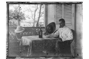 Kurt Beyer mit Fächer : Phetchaburi. Dr. Kurt Beyer mit Fächer am Tisch sitzend und lesend auf der Veranda seines Hauses, 1909