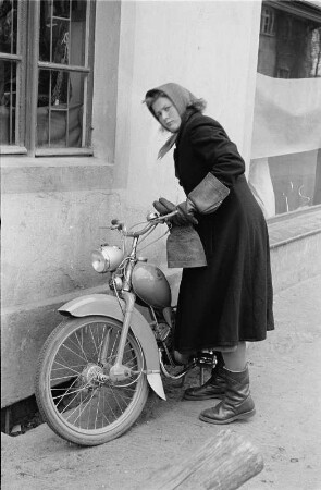 Eine junge Frau stellt ihr Moped vor einem Gebäude ab