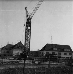 vorn Baustelle mit Zaun: Fundament mit Baukran: hinten Wohn- und Geschäftshäuser: rechts Geschäftsstelle der Deutschen Angestelltenkrankenkasse (DAK)